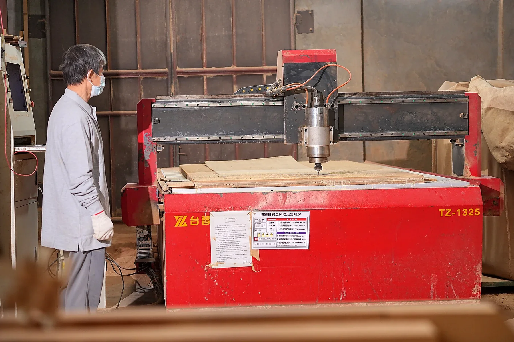 An operator beside a CNC router machining wood in a workshop